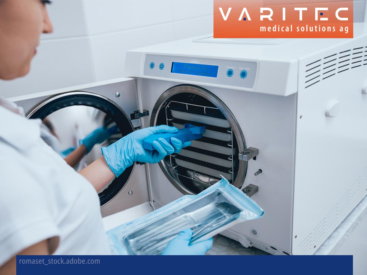 Person zieht Tablett aus Autoklav, in der anderen Hand hält sie verpackte medizinische Instrumente