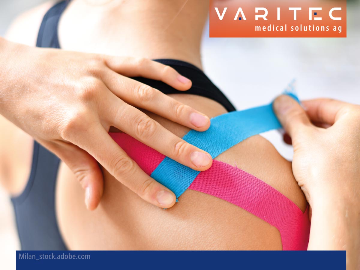 Person klebt einer Patientin einen blauen Streifen Kinesiontape auf die Schulter