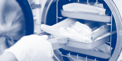 Hand mit weißen Untersuchungshandschuhen schiebt tablett mit verpackten Instrumenten in Autoklaven