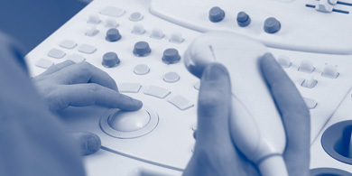Medizinisches Personal an Sonographiesystem, eine Hand bedient das Gerät, die andere Hand hält die Ultraschallsonde
