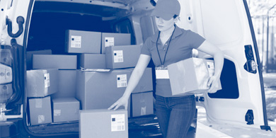 Mitarbeiterin eines Paketdienstes lädt Paket aus ihrem Auto aus