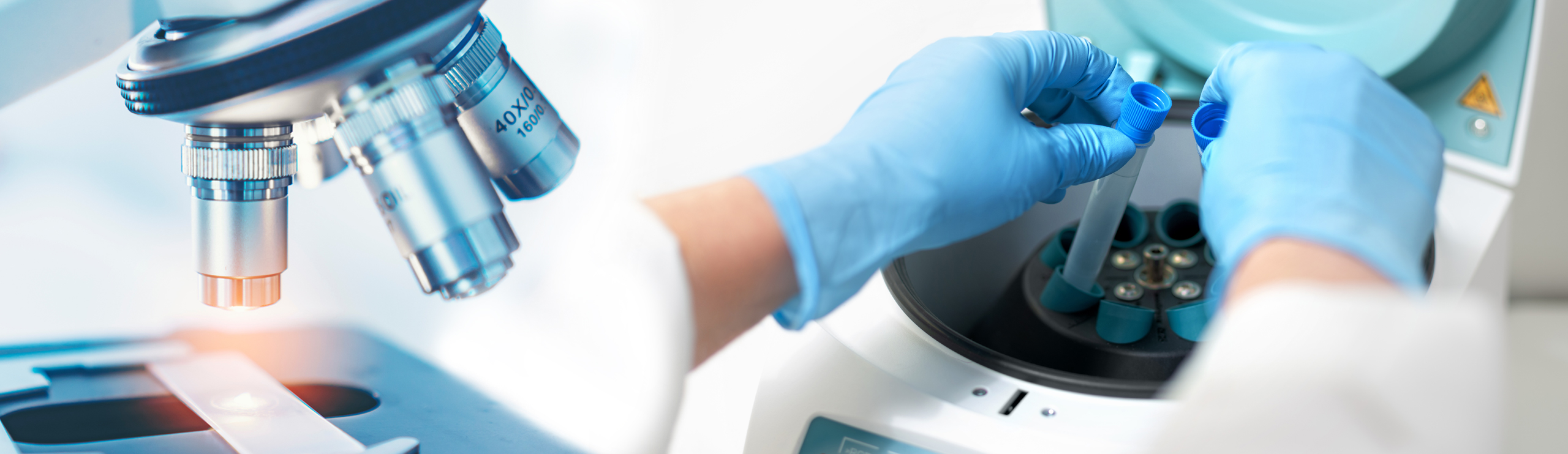 Laborgerät mit Mikroskopobjektiven und Hände in blauen Handschuhen, die Probenröhrchen in eine Zentrifuge einsetzen